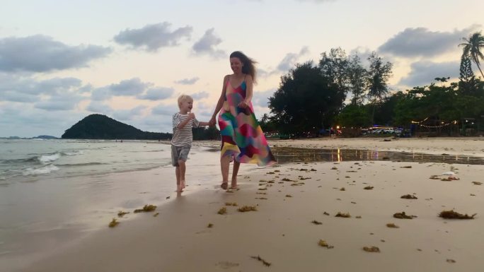 度假的傍晚，母亲和儿子愉快地在海滩上奔跑，脚浸在水里