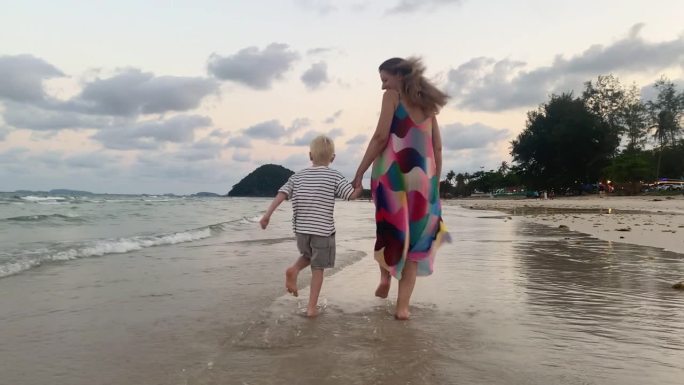 度假的傍晚，母亲和儿子愉快地在海滩上奔跑，脚浸在水里