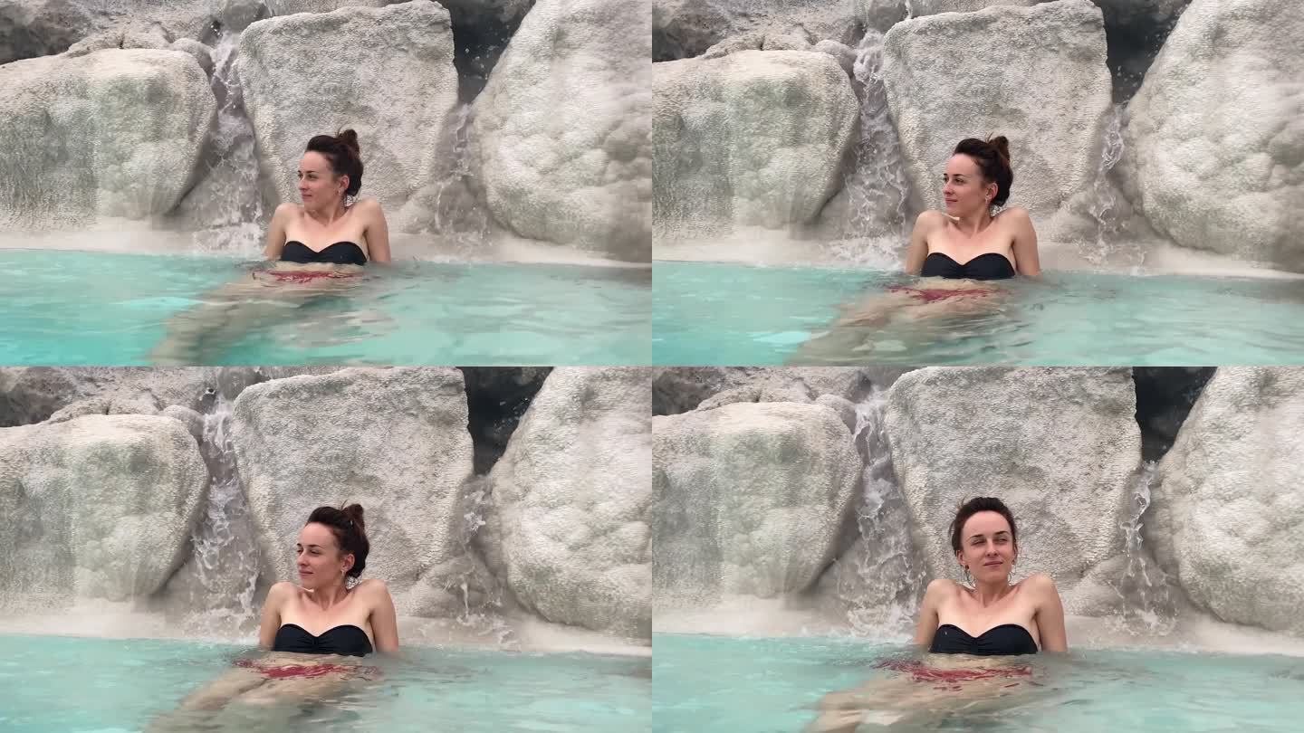 露天水疗胜地，女性在瀑布下的温泉中放松，绿松石般的水充满了具有治疗作用的硫磺泥。温泉池造福人体健康，