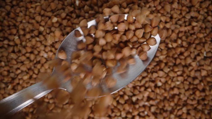 荞麦的旋转背景，荞麦从上面倒在勺子上。慢动作。