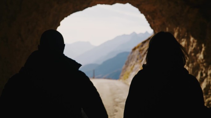 庆祝胜利:徒步旅行者的剪影交换击掌退出山隧道