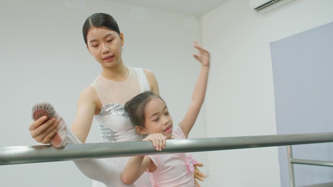 芭蕾舞老师在演播室帮助女学生在杠上伸展姿势。