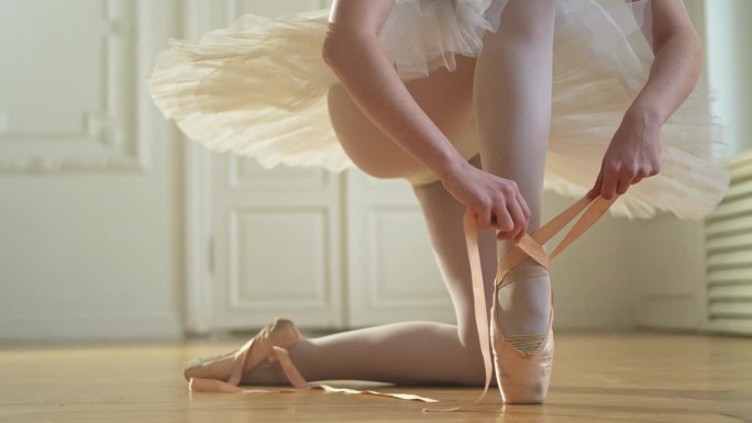 芭蕾舞女演员在舞蹈课上把脚尖鞋穿在腿上。古典芭蕾舞女演员在舞蹈工作室。芭蕾舞女演员穿上系着古典尖头鞋