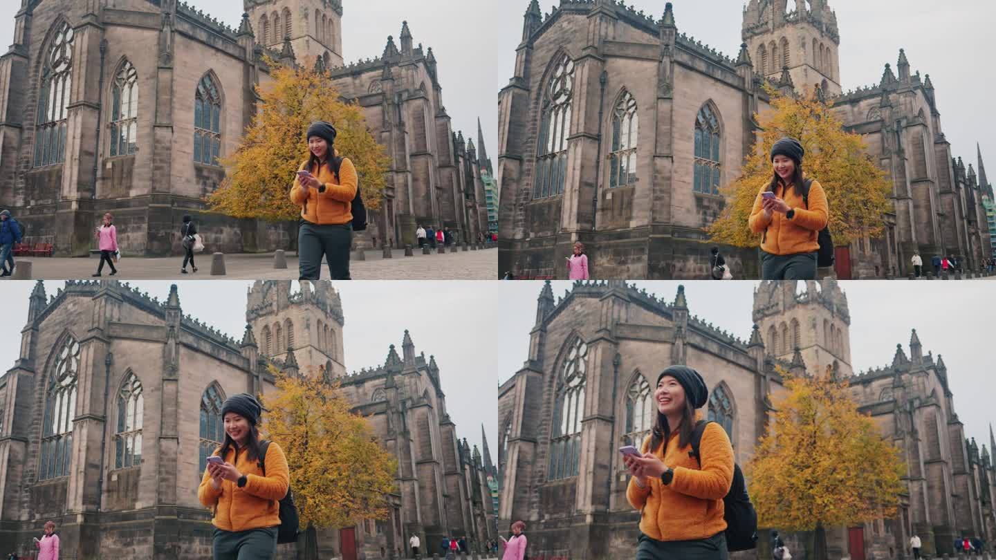 在英国苏格兰爱丁堡的老城区，一位身穿冬季外套的亚洲女行人正在用手机微笑着环顾四周