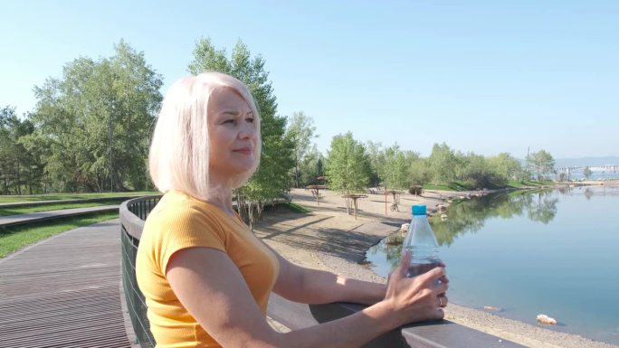 在夏季公园瑜伽后，老年妇女放松和喝水。