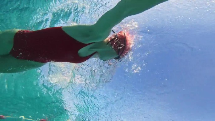 在阳光明媚的日子里，坚定的年轻女子在泳池里练习爬泳的低角度水下镜头