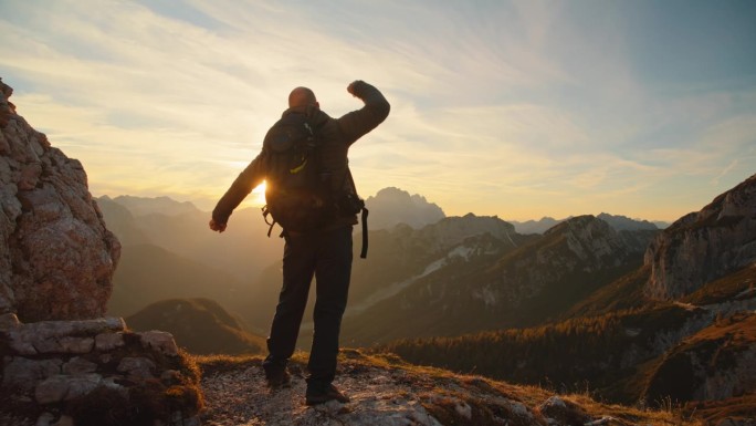 在日落时分拥抱大自然的辉煌:一个人在山顶上张开双臂，喜悦和胜利