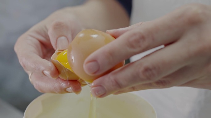女性用手敲鸡蛋，把蛋黄和蛋白分开的特写
