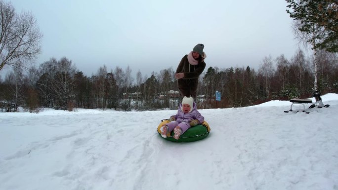 小孩子三胞胎姐妹在冬天骑在一个充气奶酪蛋糕与低雪坡