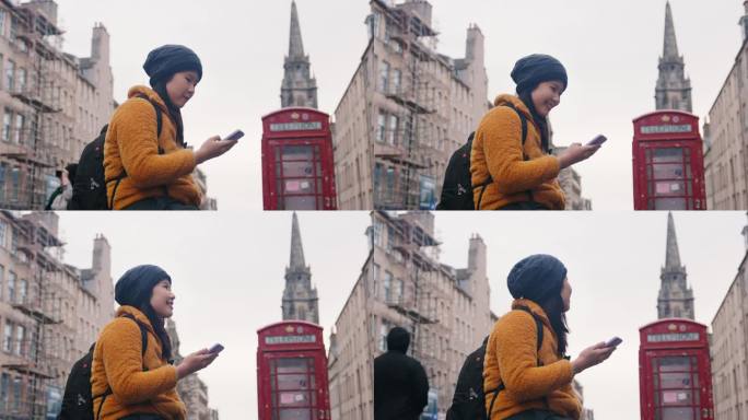 在英国苏格兰爱丁堡的老城区，一名亚洲女子穿着冬衣，拿着手机，对着红色的公用电话亭微笑，环顾四周