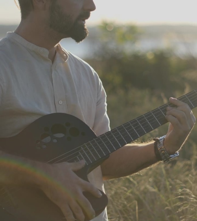 一个高加索人站在秋天的田野里，背着阳光，拿着吉他弹着和弦，唱着新歌