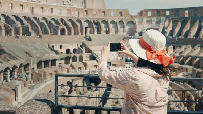 意大利罗马夏季斗兽场，亚洲女性游客观光景点的实时后景，用手机微笑拍照，四处张望
