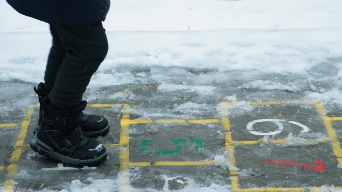 小孩子穿着靴子在外面下雪时蹦蹦跳跳。冬天的衣服，童鞋