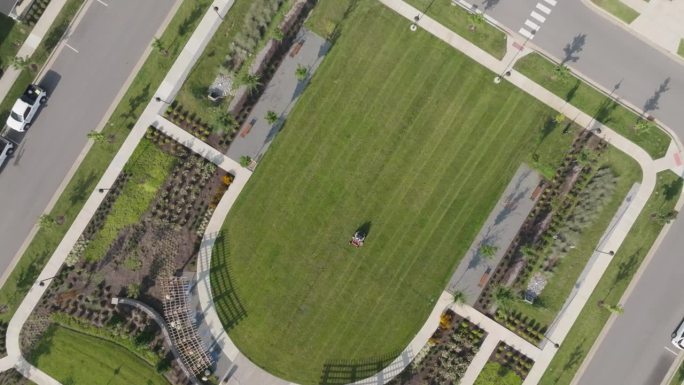 无人机拍摄的一名男子使用骑式割草机在公寓大楼附近的公园割草