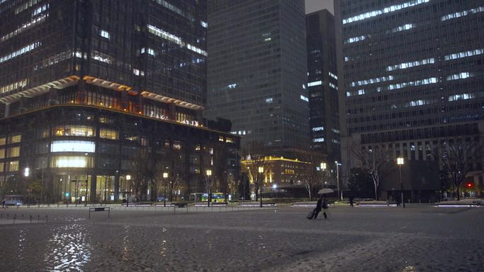 夜晚，东京的摩天大楼上飘着雪花，丸之内的行人打着伞行走