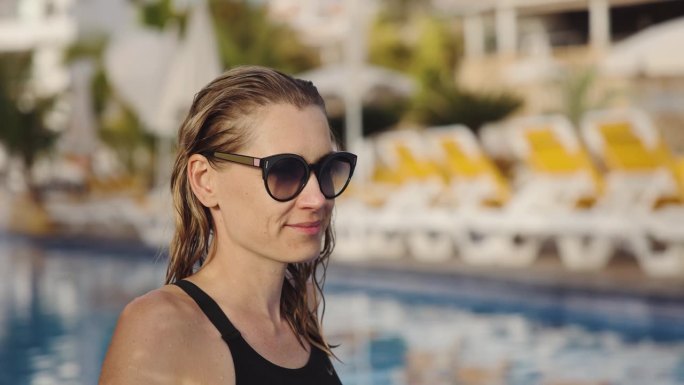 头发湿漉漉、戴着墨镜的女子在度假胜地的游泳池边放松