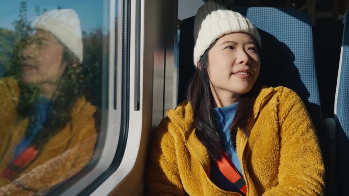 亚洲女游客早上在火车、城际公共交通上醒来，透过窗户向外看，很开心