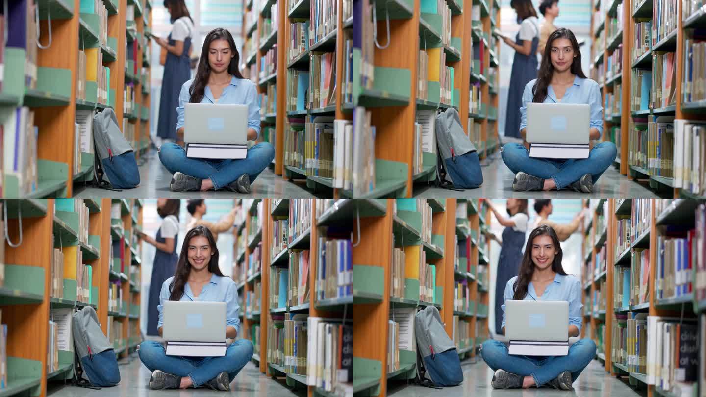 一名女学生坐在大学图书馆的书架过道里使用笔记本电脑