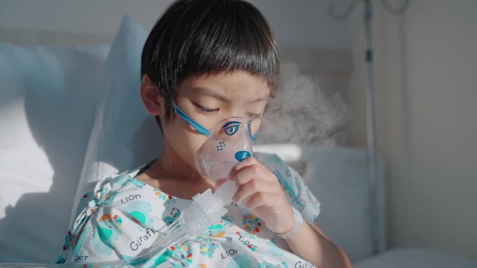 亚洲小男孩抱着一个吸入口罩，在医院的病床上从感冒中恢复过来