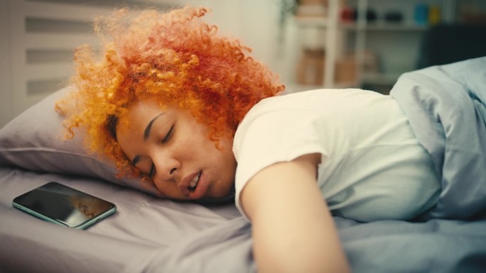 年轻的卷发女人在床上睡到早上很晚，拖延症