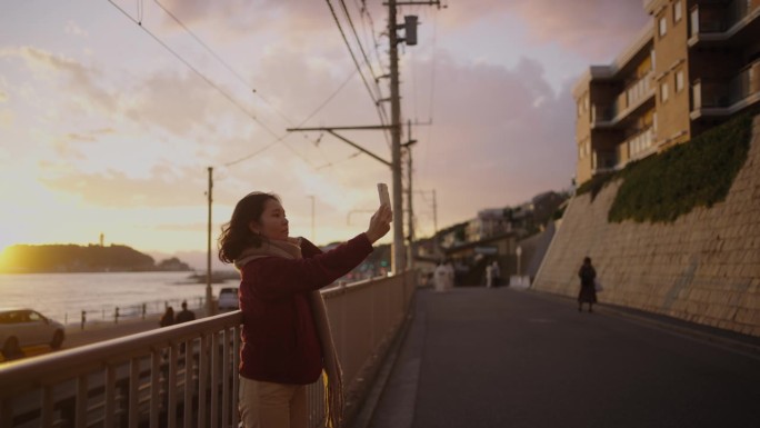 戴着围巾的年轻女子在夕阳下用手机视频通话。