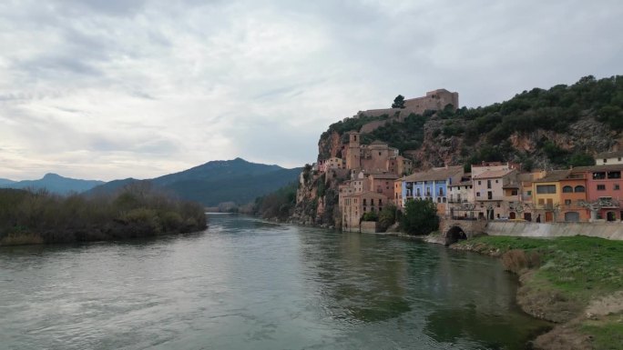 河流流经西班牙塔拉戈纳历史悠久的米拉韦特镇，背景是山脉，阴天