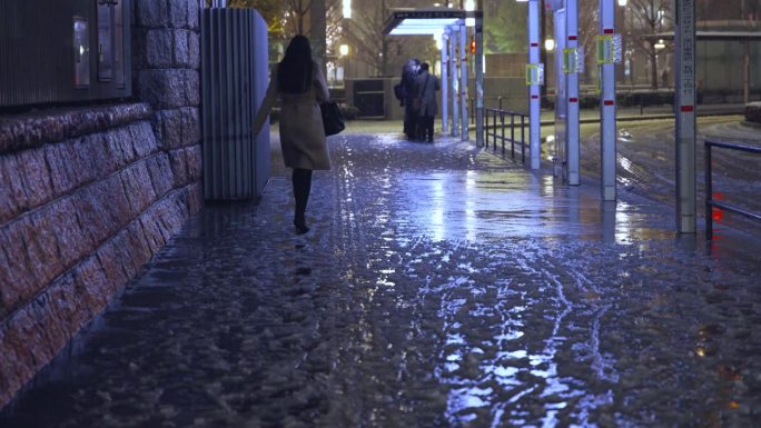 东京晚上下着雨夹雪，一名女行人独自走在丸之内的夜间街道上