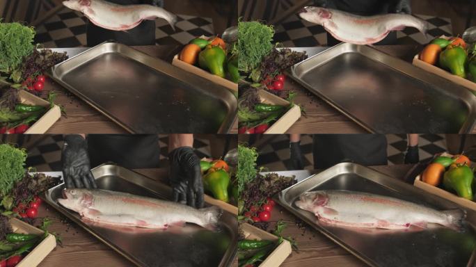厨师戴着手套，把鱼扔到托盘上，托盘上站着一桌香草和蔬菜