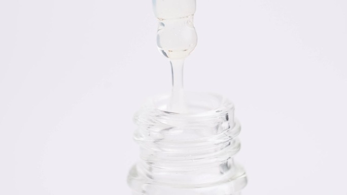 微距镜头透明保湿精华液在移液管中落入瓶中。移液器和白血清的近照。保健化妆品。