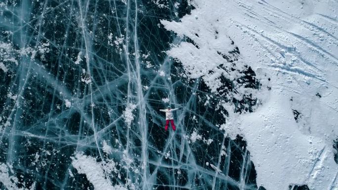 从空中俯瞰，这名年轻女子躺在贝加尔湖上裂开的蓝色冰面上，移动着她的手和腿。热门旅游景点。贝加尔湖冰冻