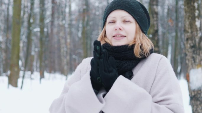 冬天的女孩在公园雪林里散步时用手搓风取暖。