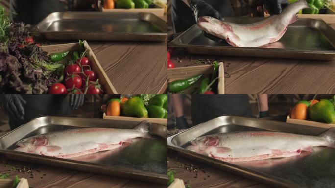 厨师戴着手套，把鱼扔到托盘上，托盘上站着一桌香草和蔬菜
