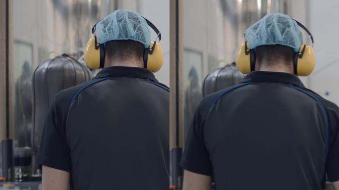一位戴着发网和耳机的操作员在啤酒厂工作的后视图。中景镜头