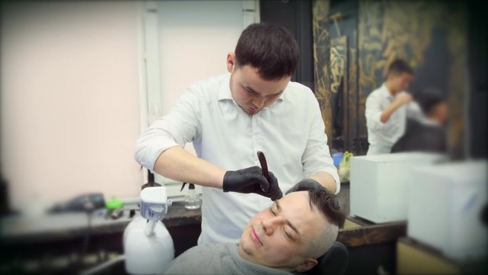 一位亚洲美发师在热气流下用直剃刀剃头