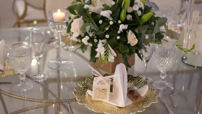 圆形玻璃桌子，中间装饰着白玫瑰和玻璃餐具。婚礼的细节