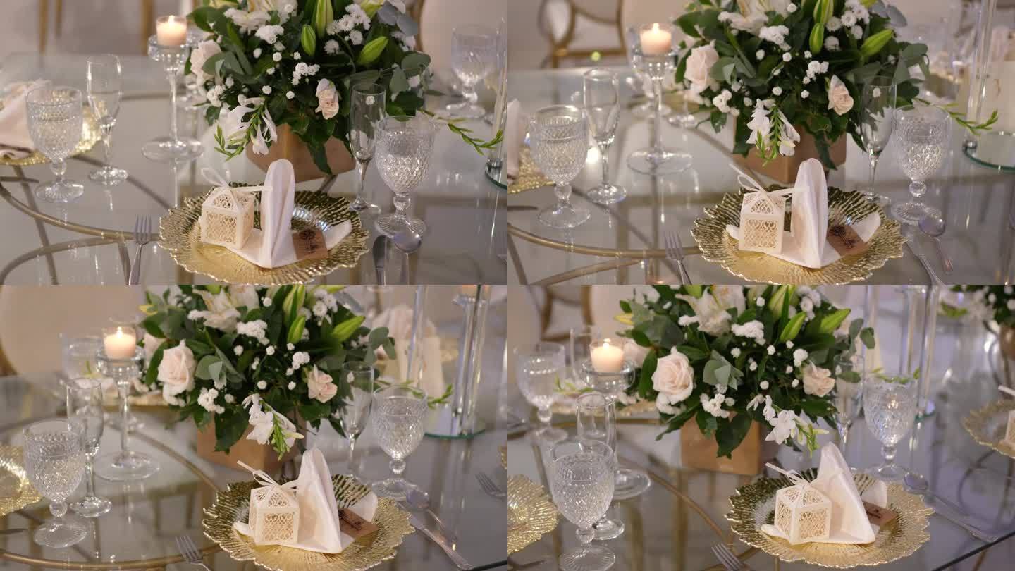 圆形玻璃桌子，中间装饰着白玫瑰和玻璃餐具。婚礼的细节