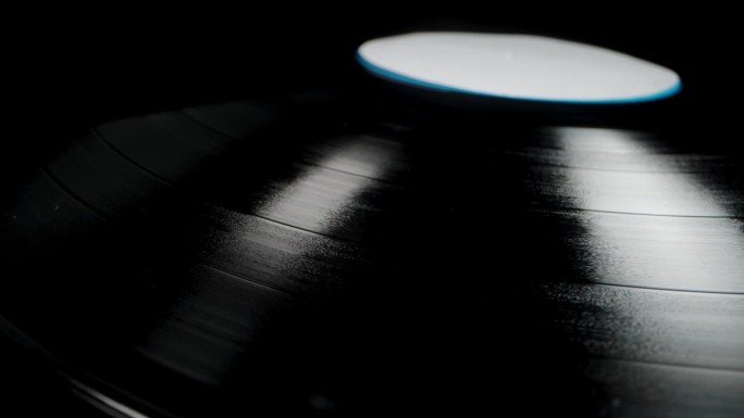 摄像机从黑胶唱片上方滑动，露出它的音频凹槽。黑色背景的特写。
