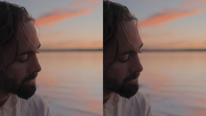 深思熟虑的蓄着胡子的潮人在湖边对着夕阳的天空弹着原声吉他——慢镜头肖像