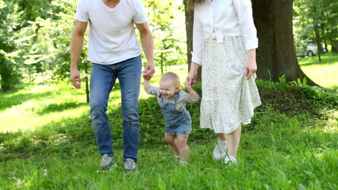 孩子牵着父母的手在公园的草地上散步，学会走路，迈出人生的第一步。幸福的家庭