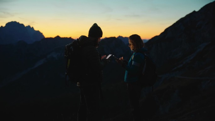 SLO MO在数字领域的导航:黄昏时分，爱冒险的夫妇在山顶上使用技术