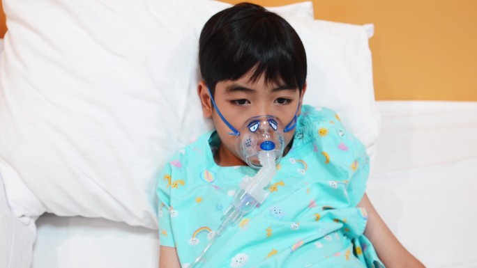 小男孩在医院病床上用面罩吸氧的特写肖像。