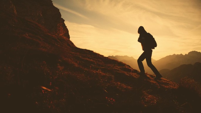 山顶剪影:黄昏时，孤独的女徒步者登上长满草的山坡