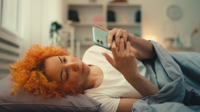 悲伤的女人躺在床上看手机里的伤人短信，网络欺凌