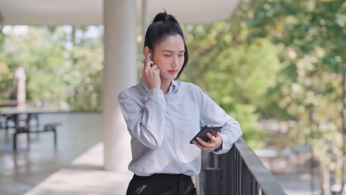 年轻的女商人在办公室外用带无线耳机的智能手机打电话