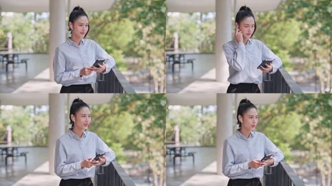 年轻的女商人在办公室外用带无线耳机的智能手机打电话