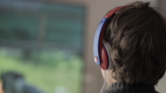 戴着耳机的男孩在主机上玩电脑多人视频游戏。儿童玩家在电视屏幕上玩电子游戏。戴着耳机和操纵杆的人在大电