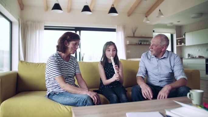 一个小女孩和上了年纪的祖父母在室内演奏竖笛。