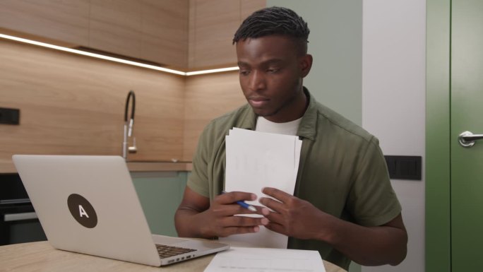 用笔记本电脑处理文件的黑人。30多岁的企业家在家办公室管理文件、发票、税单。