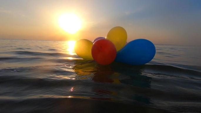 在一个阳光明媚的夏日，一束五彩缤纷的气球在海浪上摇摆。清晨，黄昏，日落，黎明，许多彩色的小气球绑在一