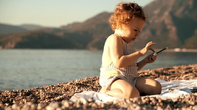 有趣的小女孩在海滩上的现代手机上滚动应用程序